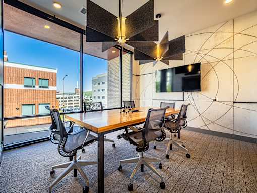 A conference room with a long table and chairs, a television, and a view of the cityscape outside the window.