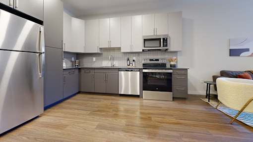 A modern kitchen with a refrigerator on the left and a dining area with a chair and table on the right.