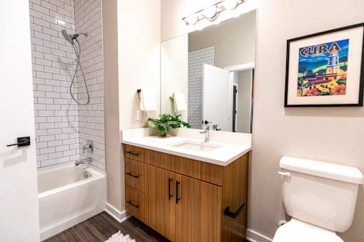 A bathroom with a white toilet, a white sink, a white bathtub, and a wooden cabinet. at The Hive Apartments, Allentown, PA