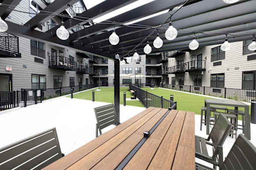 A wooden table is in the foreground of a patio with chairs and a view of apartment buildings.