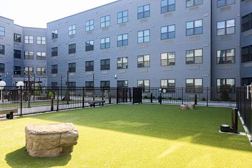 A large rock sits in the middle of a green play area in front of a grey building.