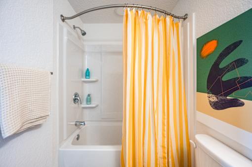 A bathroom with a white tub and a yellow shower curtain.at The Teale Golden Gate in Naples, FL, 34116
