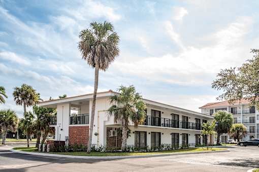 A white building with a balcony and a palm tree in front.at The Teale Golden Gate in Naples, FL, 34116