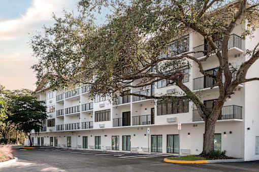 A large white building with balconies and a tree in front.at The Teale Golden Gate in Naples, FL, 34116