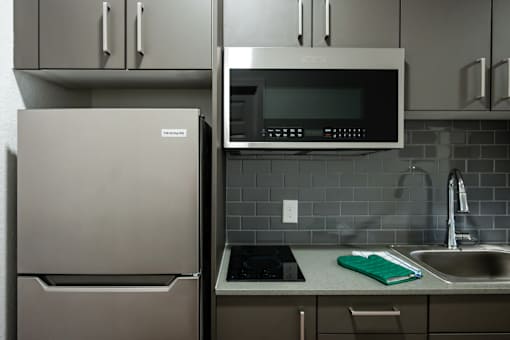 A kitchen with a refrigerator, microwave, and sink.