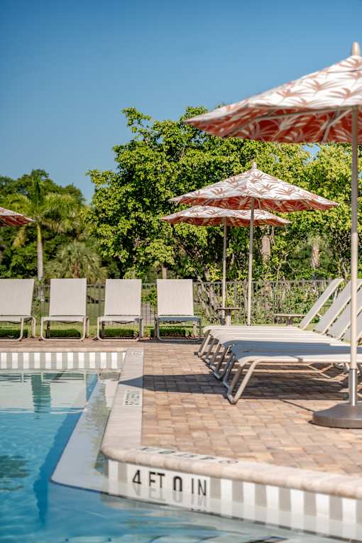 A pool with a 4 foot deep sign and chairs under umbrellas.