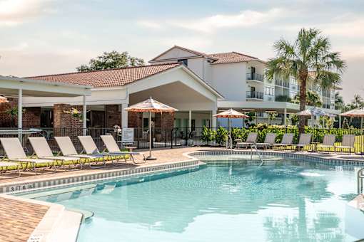 A pool area with sun loungers and a building in the background.