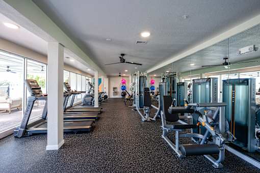 A spacious gym with treadmills, exercise machines, and a ceiling fan.