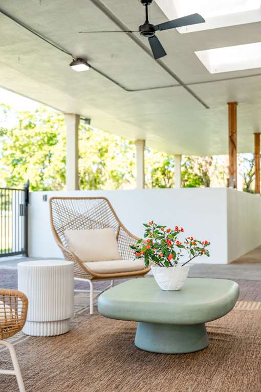 A white chair with a woven back is placed on a green table with a white vase of flowers on it.