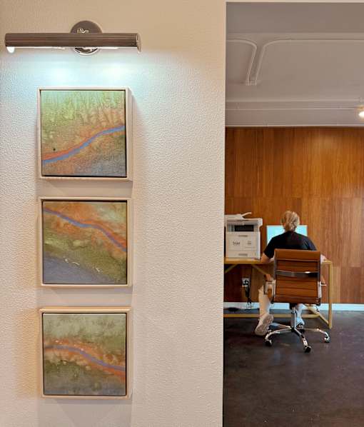 Three landscape paintings are hanging on a white wall.
