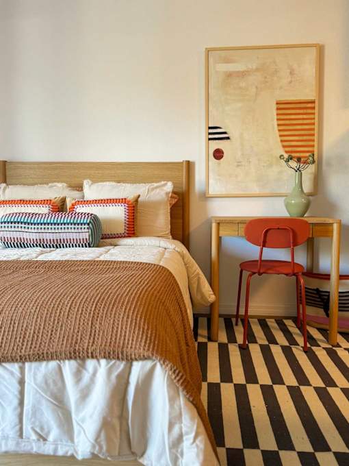 A bed with a brown blanket and a red chair in front of a painting. at The Teale Golden Gate in Naples, FL, 34116