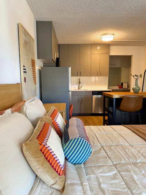 A bed with pillows in front of a kitchen. at The Teale Golden Gate in Naples, FL, 34116