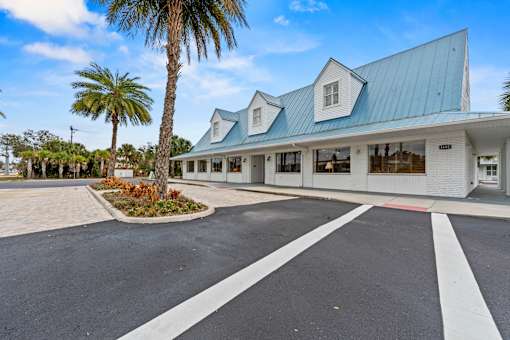 A white building with a blue roof and a palm tree in front.
