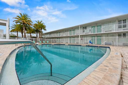A swimming pool in front of a building with palm trees.