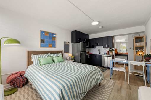 A bedroom with a bed, a desk, and a kitchen area.