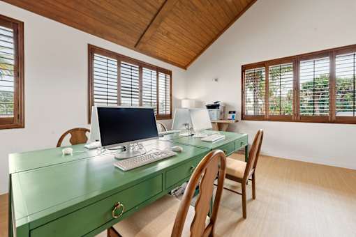 A green desk with a computer on it in a room with wooden ceiling and windows.