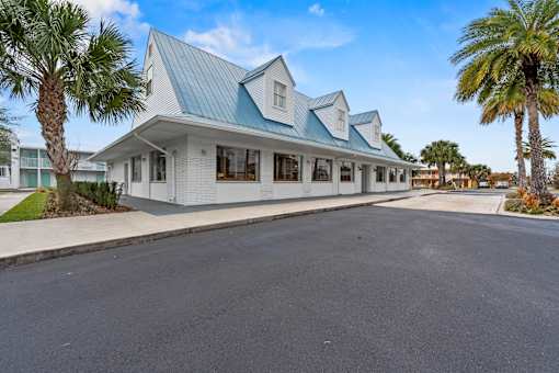 A white building with a blue roof is surrounded by palm trees.