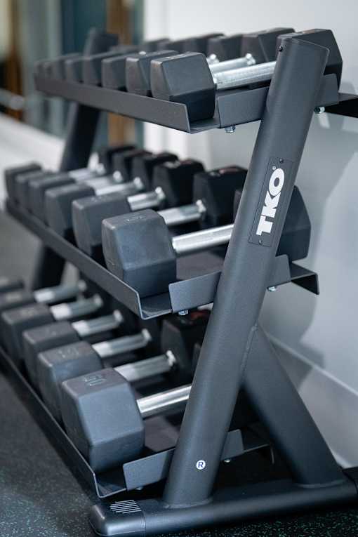 A close up of a TKO branded dumbbell rack with grey dumbbells.