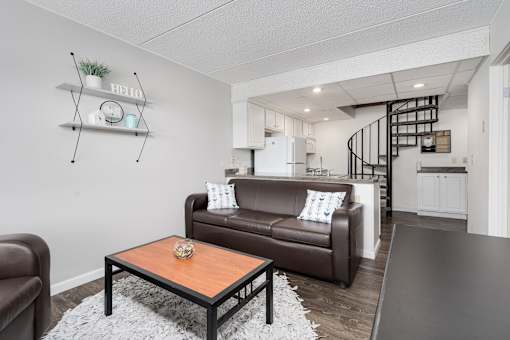 A living room with a brown leather couch, a coffee table, and a spiral staircase in the background.