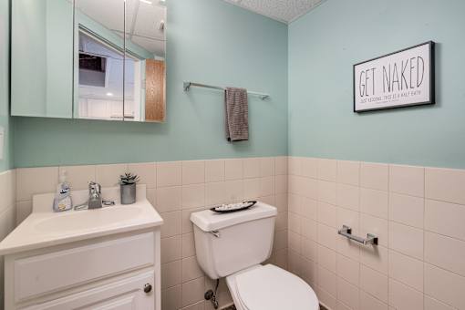 A bathroom with a toilet, sink, mirror, and a sign that says "Get Naked".