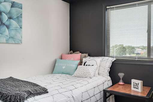 A bedroom with a bed, pillows, a blanket, and a small table with a sign on it.