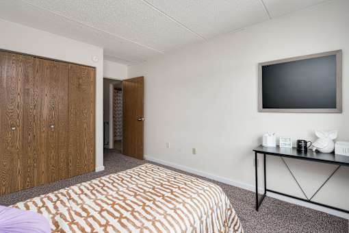 A bedroom with a bed, a table with a TV on it, and a wooden wardrobe.