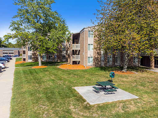 A green picnic table sits in the middle of a grassy area in front of a building.
