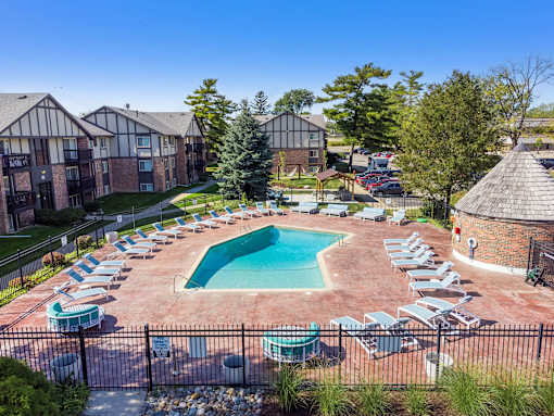 A pool surrounded by chairs and trees in front of apartment buildings.