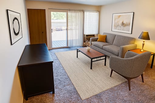 A living room with a grey couch, a brown chair, a brown coffee table, and a brown cabinet.