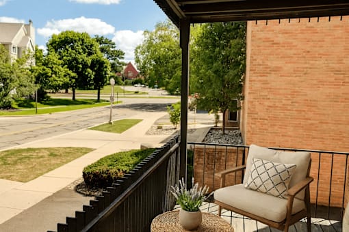 A balcony with a chair and a pillow overlooking a street.