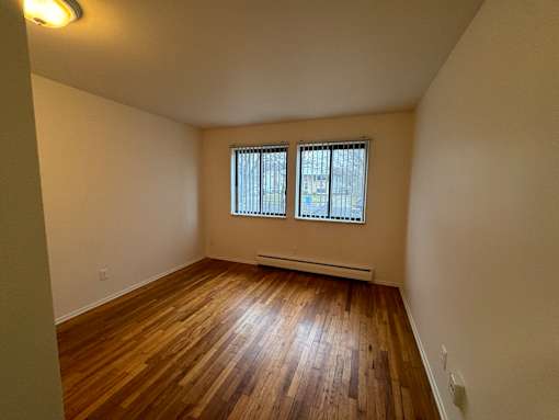 An empty living room with wooden floors and two windows
