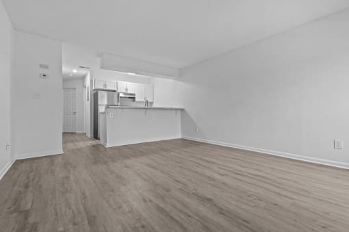 the living room and kitchen of an apartment with white walls and wood flooring