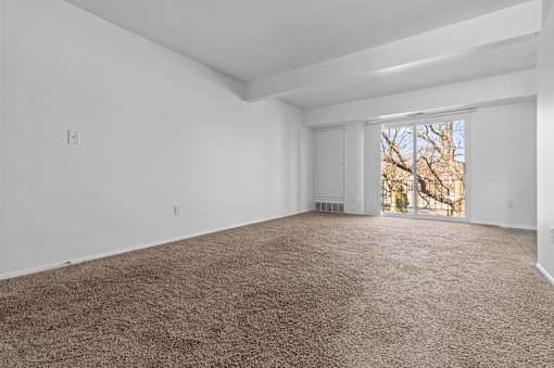 a living room with white walls and carpet and a window