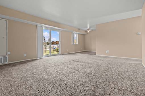 A room with beige walls and a carpeted floor with a sliding glass door leading outside.