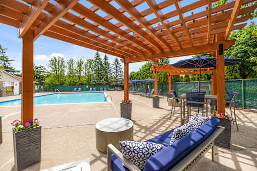 A wooden pergola over a poolside seating area.