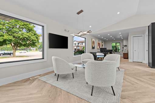 A modern living room with a large window, a flat screen TV, and a set of white chairs. at Park On Canal Apartments - Clinton Twp, MI Apartments, Apartments, Clinton Twp, MI