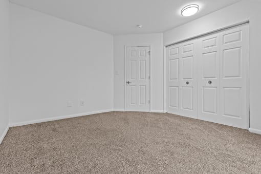 an empty bedroom with white doors and carpeting