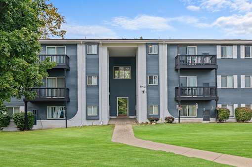 the view of a blue apartment building with a green lawn