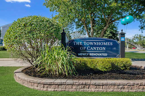A sign that says "The Townhomes of Canton Newly Renovated" is displayed in front of a landscaped area.
