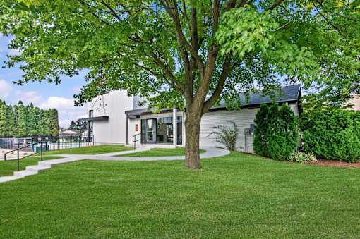A tree in front of a building with a white fence in the background at Park On Canal Apartments - Clinton Twp, MI Apartments, Michigan, 48038