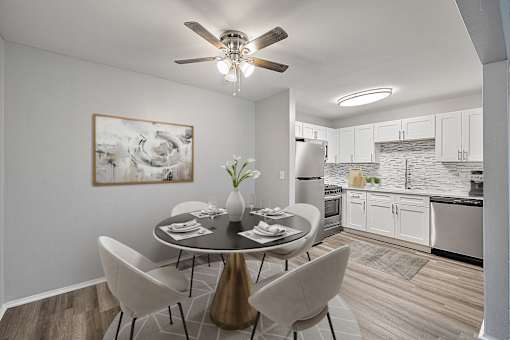 A modern dining room with a table set for two and a kitchen in the background.