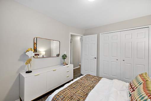 A white bedroom with a bed, dresser, and mirror.