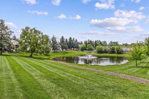 A serene landscape with a pond, trees, and a clear sky.