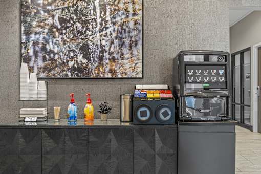 A black and white painting hangs on a wall above a counter with a soda machine and a stack of cups.