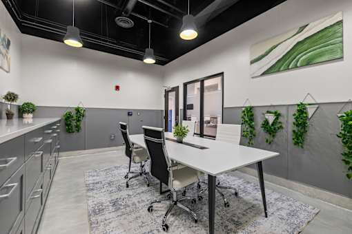 A modern office space with a white desk, black chairs, and greenery on the walls.