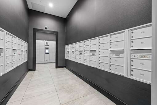 A hallway with a series of mailboxes on the wall and a door at the end.