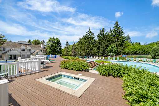 A wooden deck with a hot tub and a pool in the background.