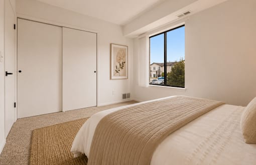A bedroom with a large bed and a window overlooking a residential area. at Park On Canal Apartments - Clinton Twp, MI Apartments, Clinton Twp, 48038