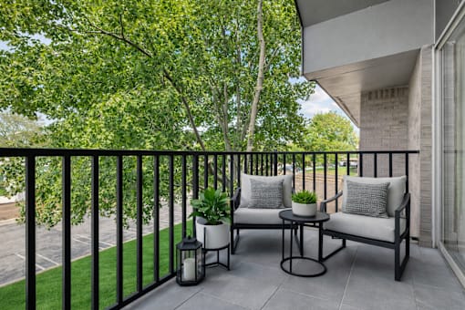 A balcony with two chairs and a table with a plant on it.