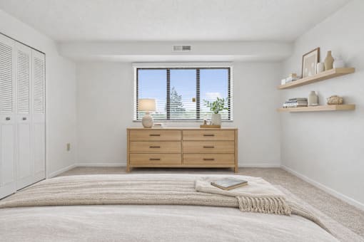A bedroom with a large bed, a window with blinds, and a wooden dresser.
